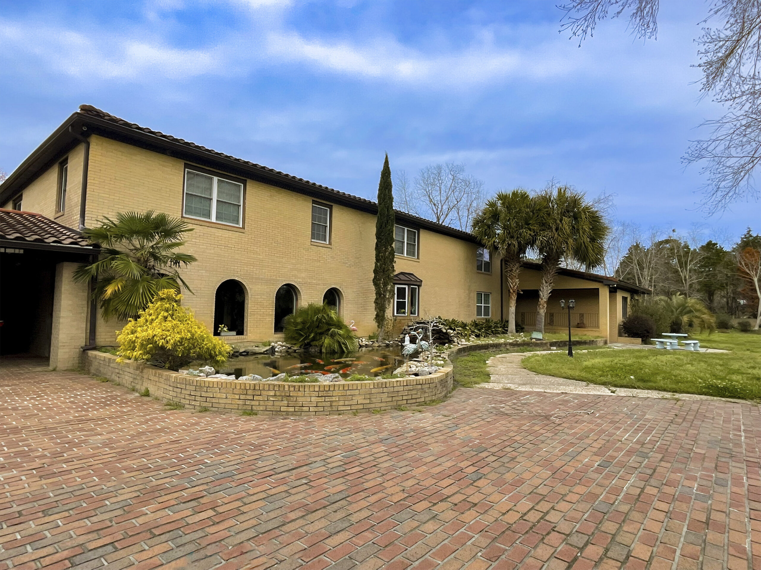 Front exterior of Palazzo Guest House with brick driveway, pond, and palm trees