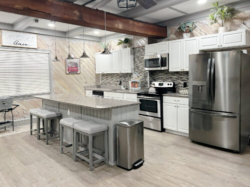 Fully equipped kitchen with granite island, bar seating, stainless steel appliances, and reclaimed wood accents at Palazzo Guest House in Leland, NC