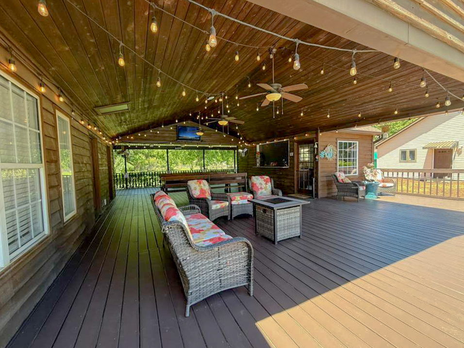 Spacious covered porch with wicker lounge seating, fire pit table, ceiling fans, and string lights at Palazzo Guest House in Leland, NC