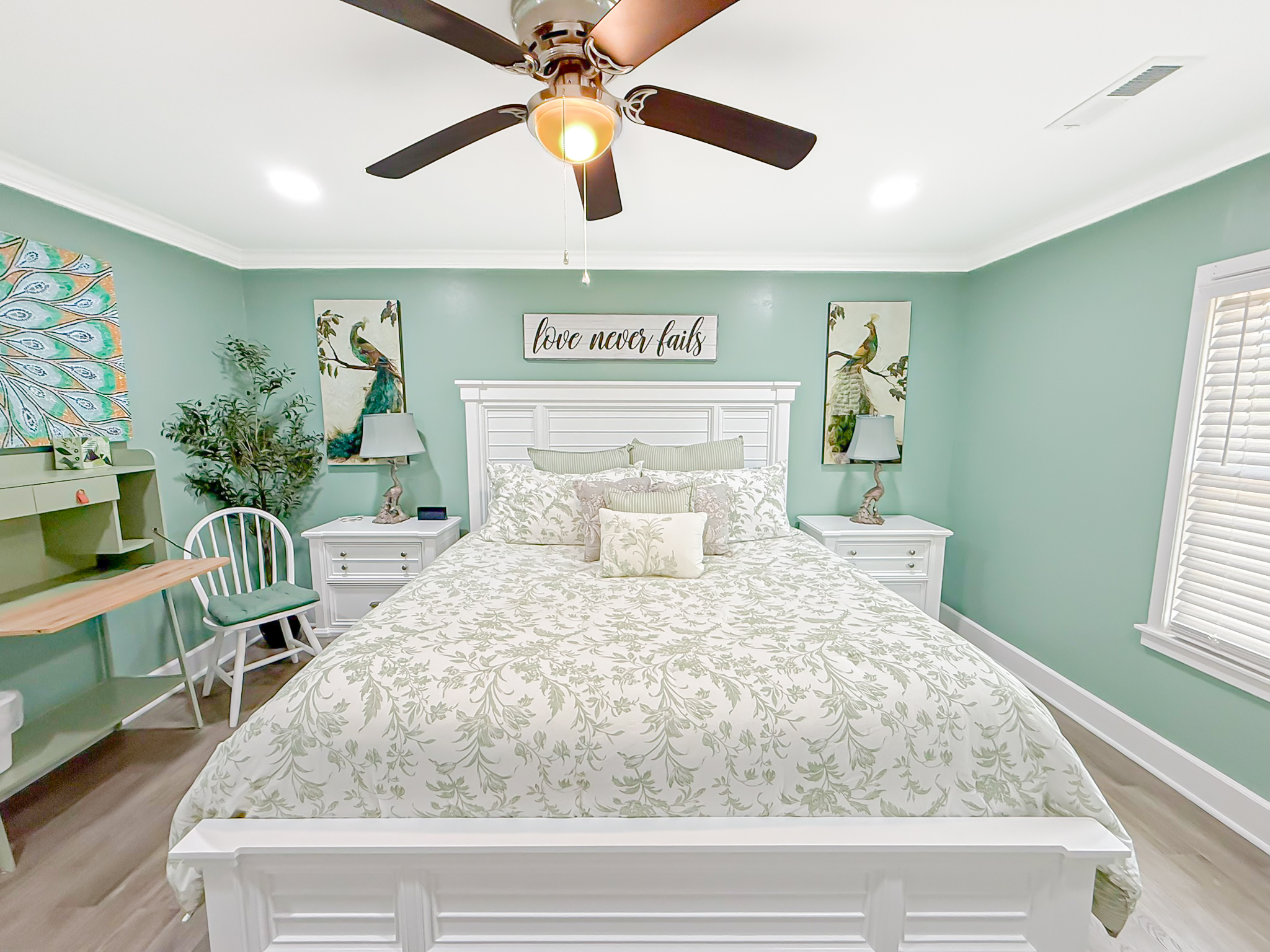 Peacock Suite bedroom with king bed, soft green walls, white furniture, and peacock artwork at Palazzo Guest House