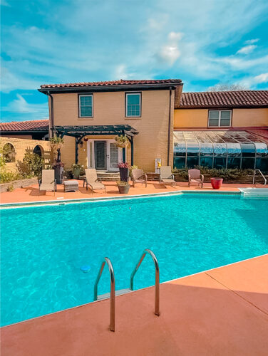 Private pool with poolside lounge chairs facing the Mediterranean-style villa and sunroom at Palazzo Guest House in Leland, NC